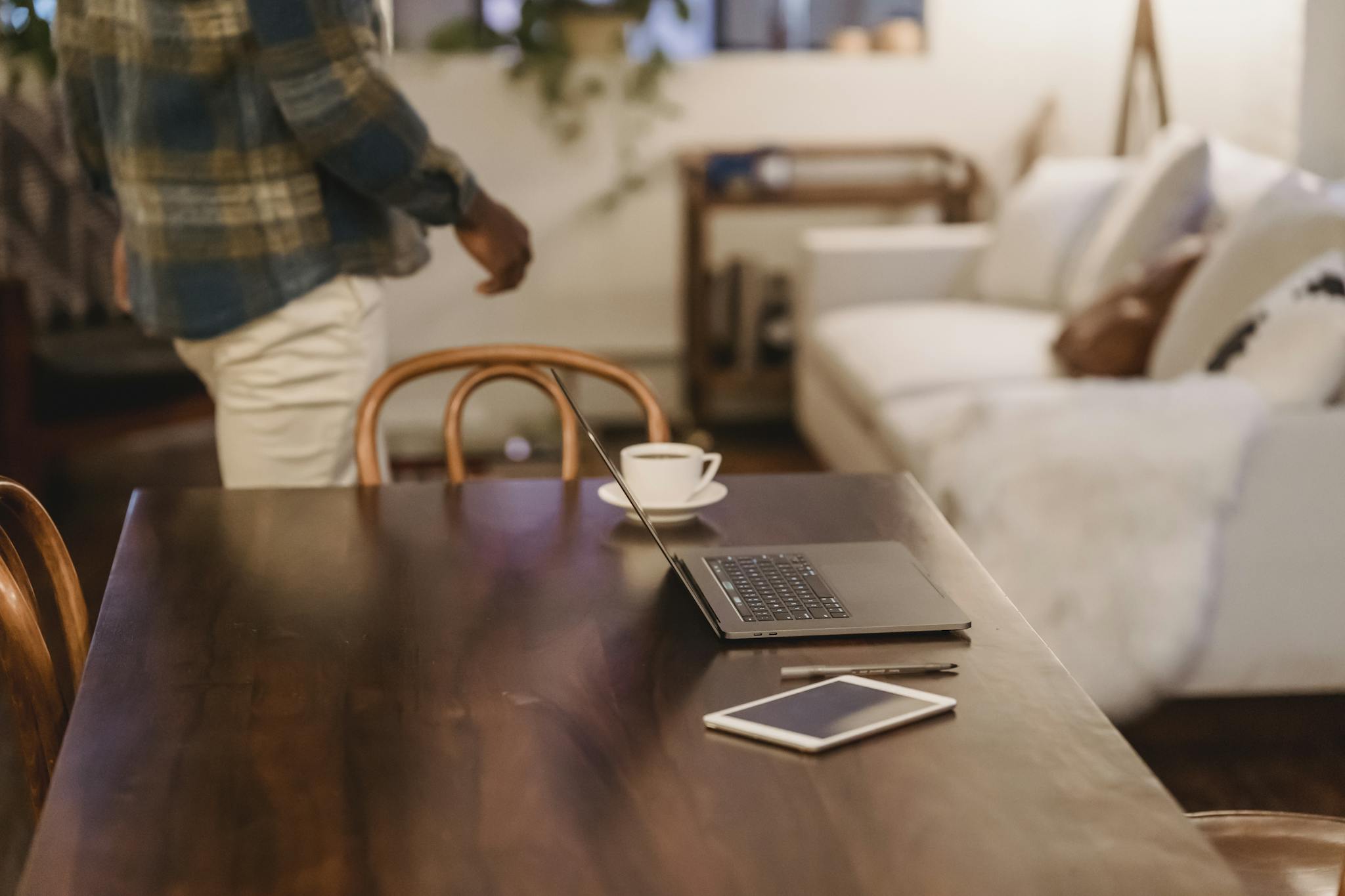 Crop anonymous black male freelancer in casual clothes walking near table with laptop and cup of coffee at home