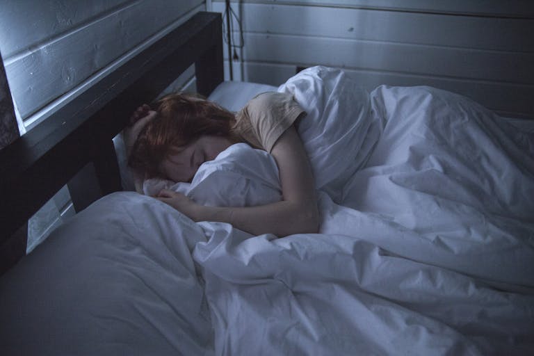 A woman sleeping peacefully in a cozy bedroom, enveloped by soft white sheets, under the gentle glow of night lighting.