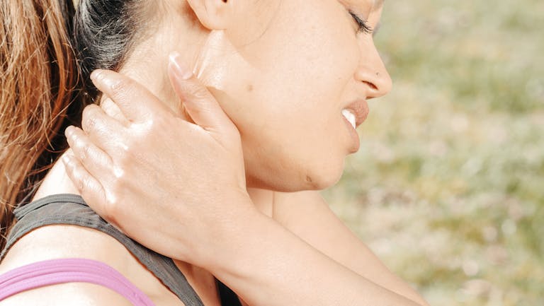 Close-up of a woman experiencing neck pain while outdoors. Health concept photo.