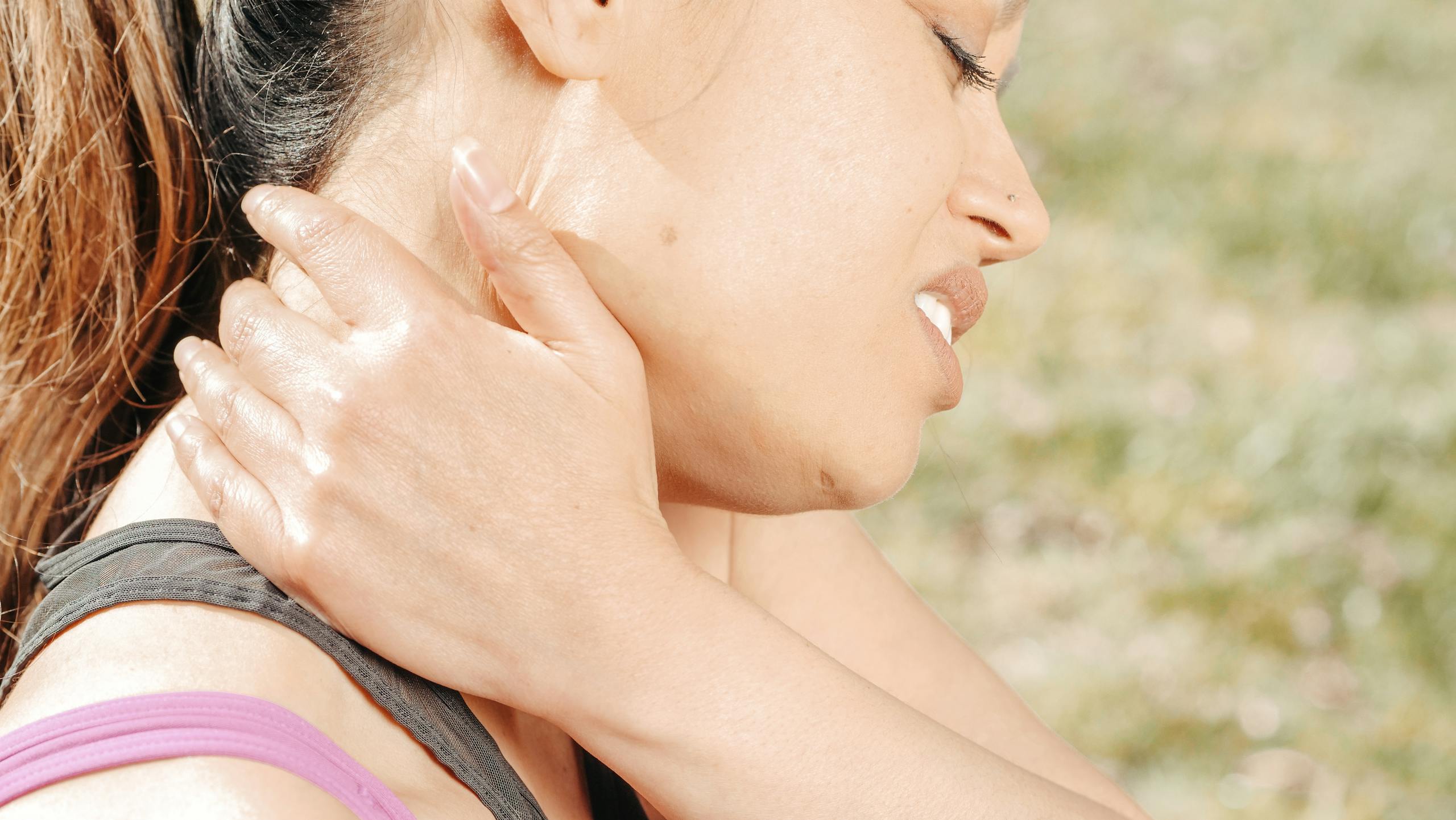 Close-up of a woman experiencing neck pain while outdoors. Health concept photo.