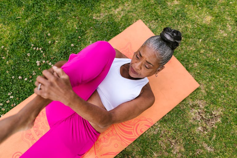 Elderly woman performing yoga stretch on grass for wellness.