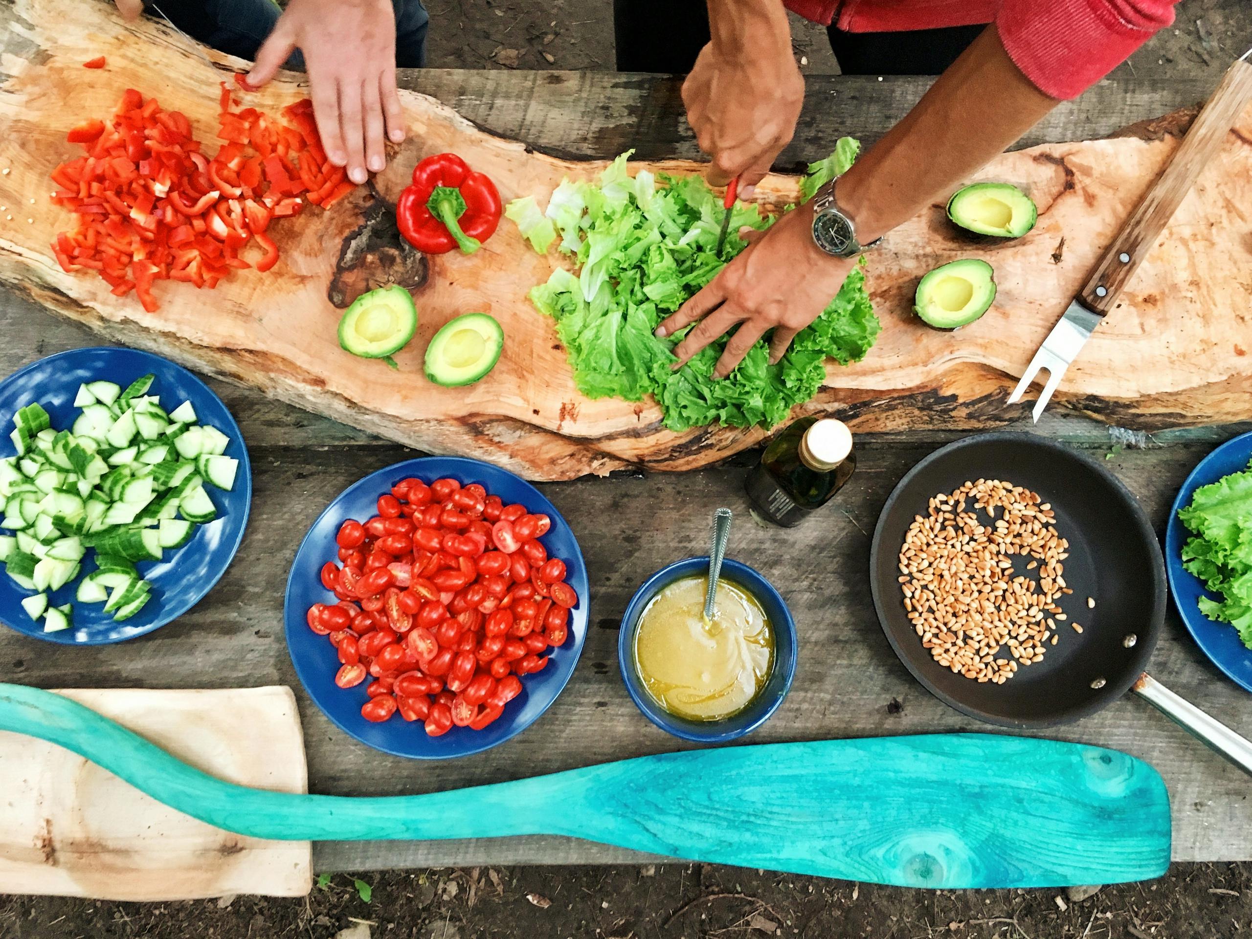 Fresh ingredients being prepared on a rustic wooden table, showcasing vibrant vegetables and hands at work.