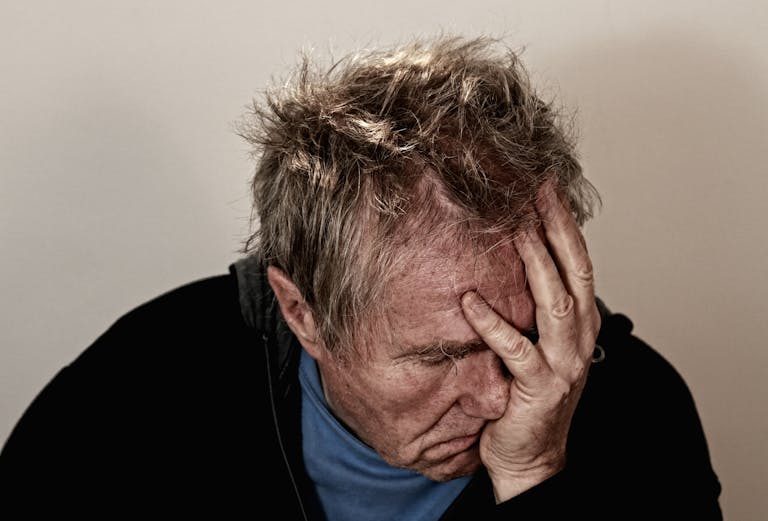 Portrait of an elderly man feeling stress and disappointment, holding his head in his hands.