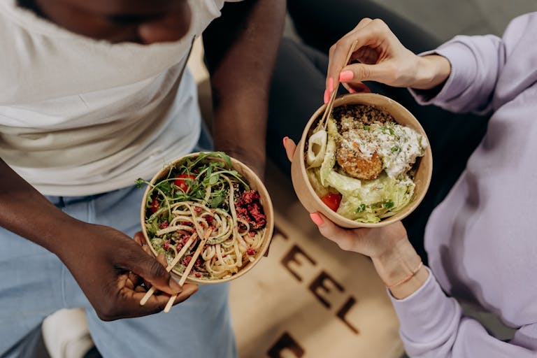 Two people holding bowls filled with salad and pasta, emphasizing healthy lifestyle choices.