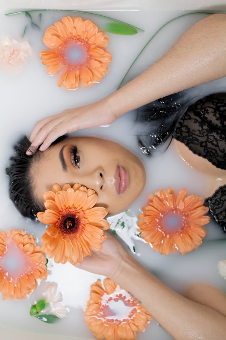 Woman in a black lace top relaxing in a milk bath with orange flowers.