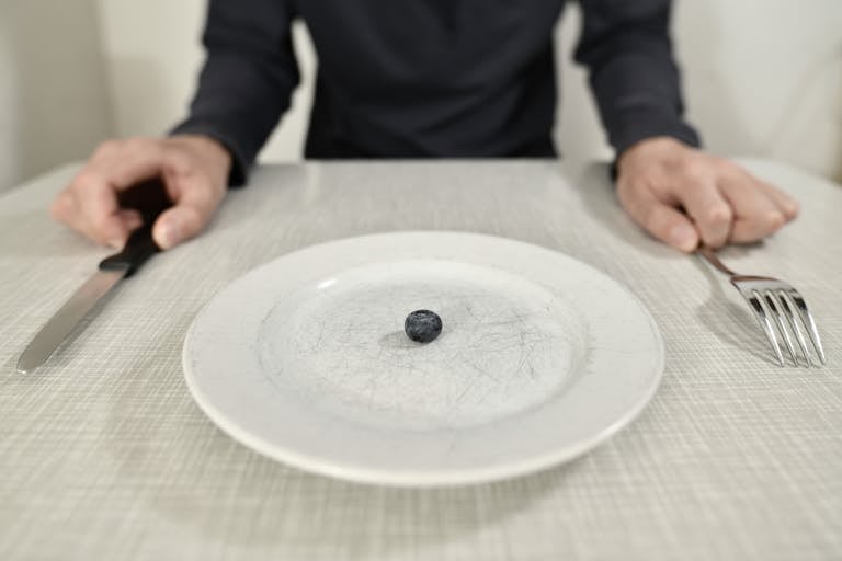 A single blueberry on a scratched plate symbolizes minimalist diet and portion control.