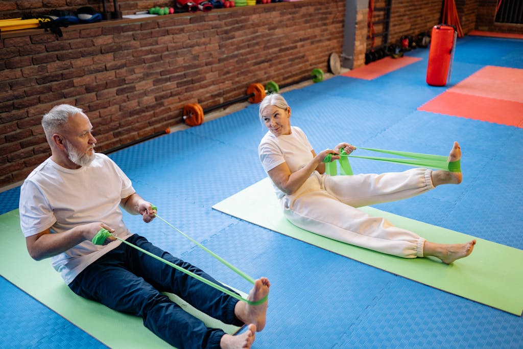 Active senior couple enjoying a resistance band workout on yoga mats in a gym setting.