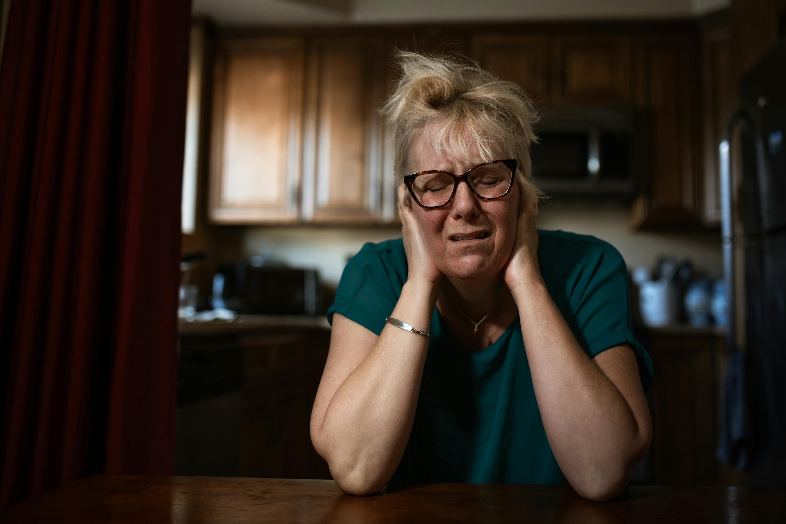 An adult woman in distress sitting at a table indoors, conveying emotional struggle.