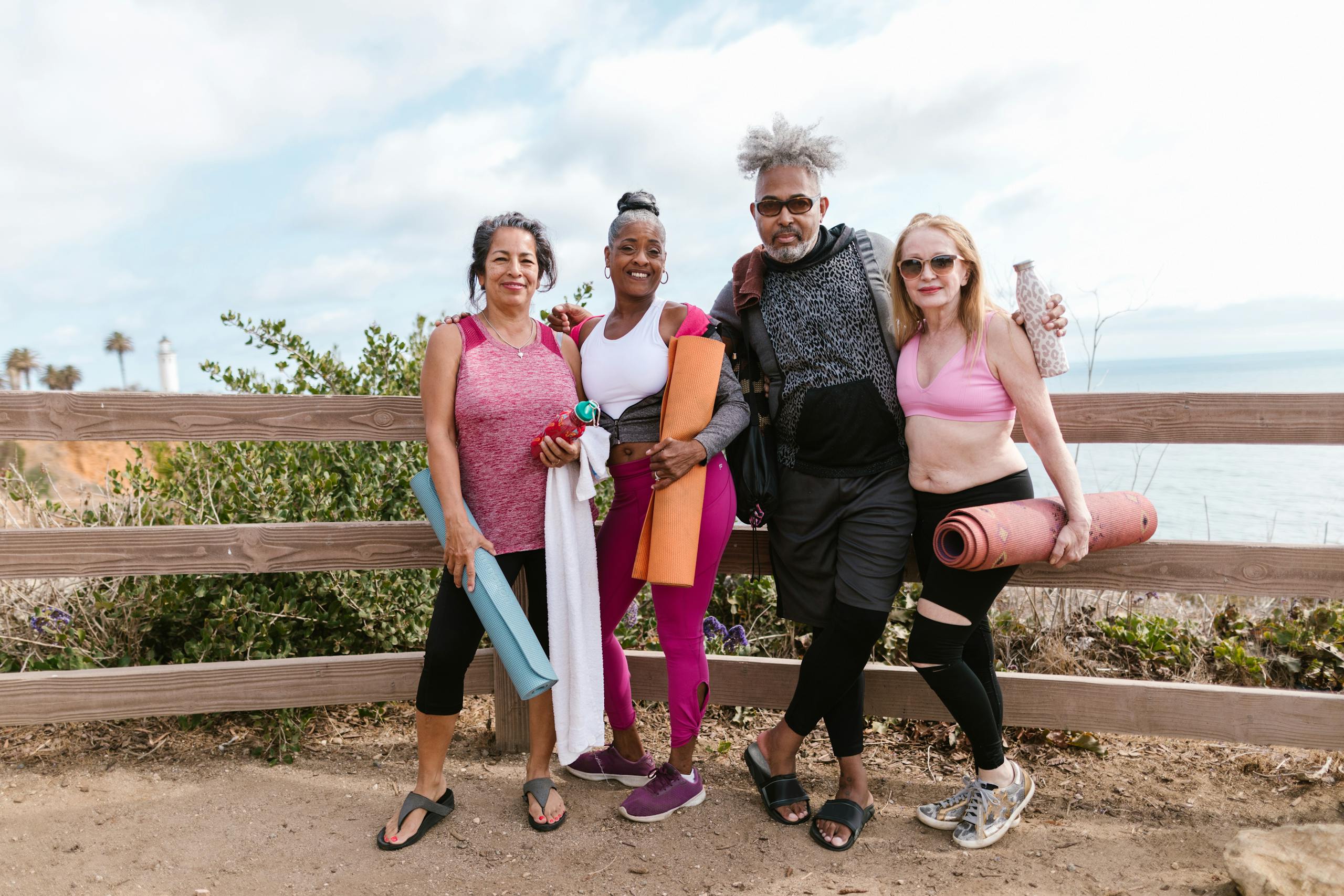 Four seniors holding yoga mats, embracing wellness by the seaside.