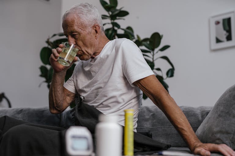 Senior man in white shirt drinking medicine indoors. Health and wellness lifestyle.