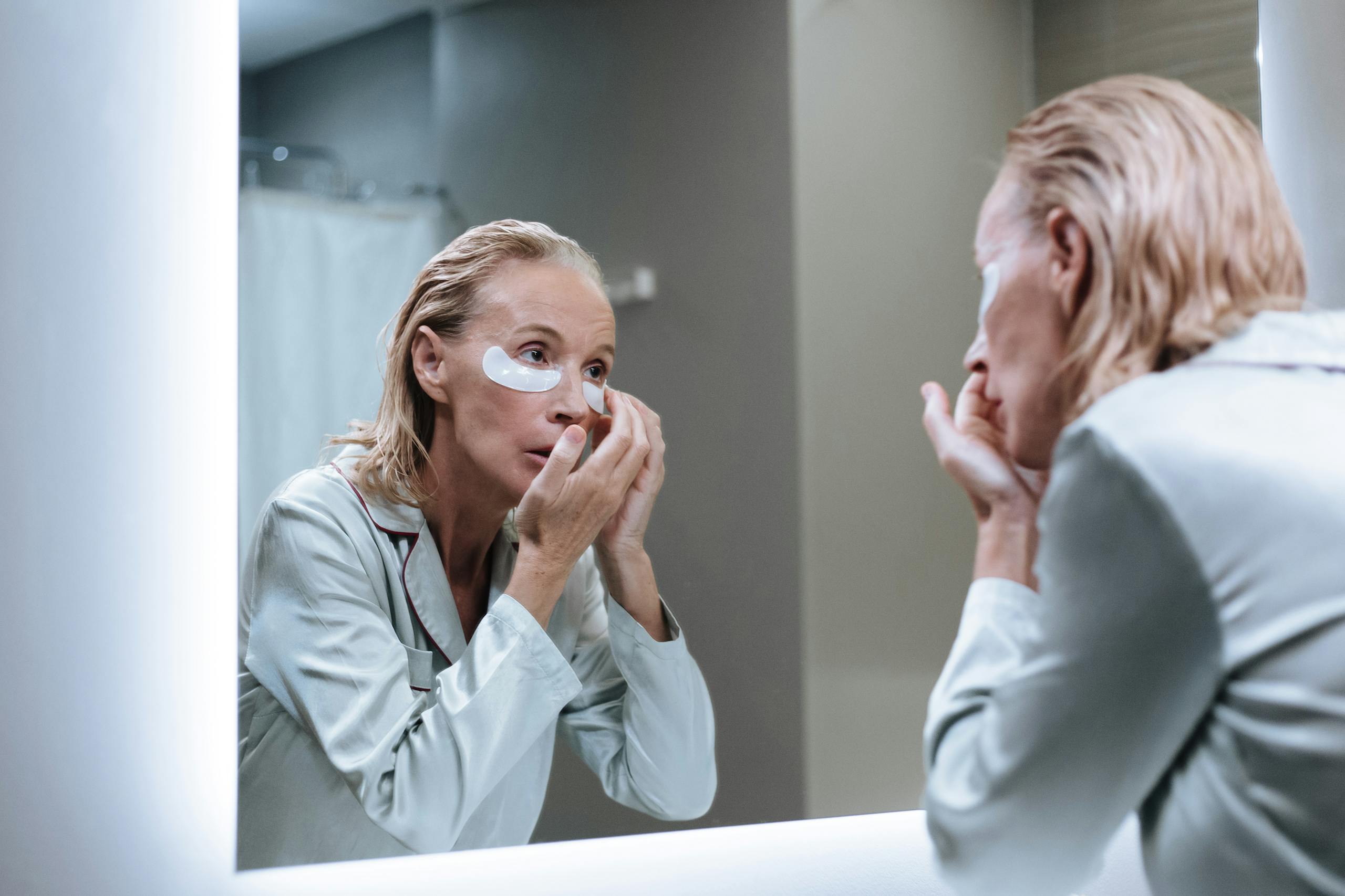 Senior woman applying eye patches during her morning skincare routine.