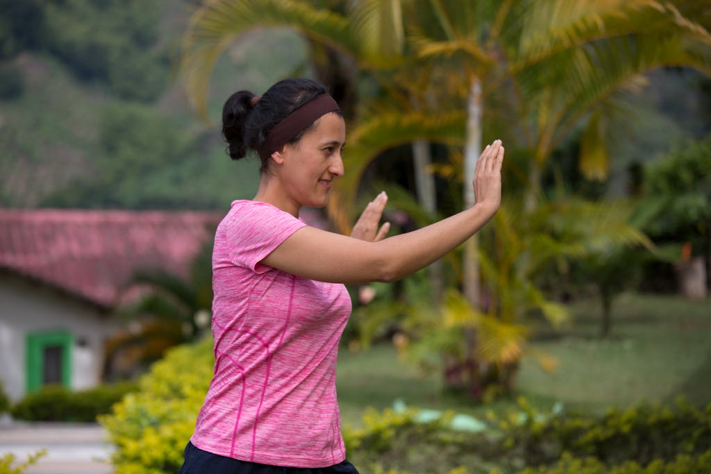 Woman performing Tai Chi outdoors, promoting a healthy lifestyle amidst lush greenery.