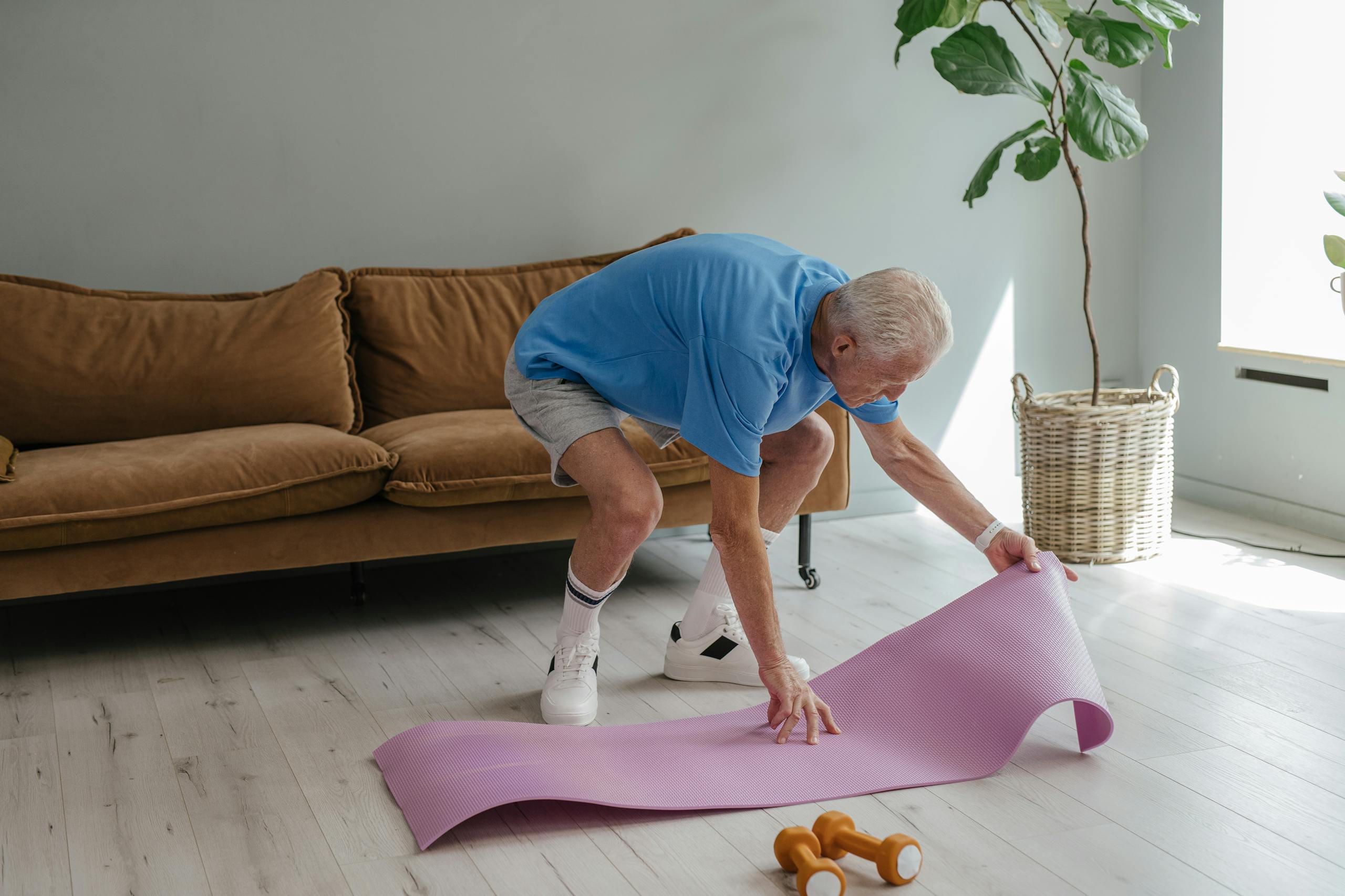 An elderly man sets up his yoga mat indoors, embodying a healthy lifestyle.